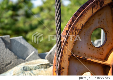Steel cable and winch. Part of an old winch with a steel rope on a lift. Detail of the cableway. Close-up view of steel big wheel of cableway in mountains against the blue sky. Steel cable and winch. Part of an old winch with a steel rope on a lift. Detail of the cableway. Close-up view of steel big wheel of cableway in mountains against the blue sky. 74655785