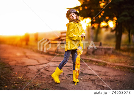 Happy funny child girl with umbrella in rubber boots at autumn park at sunset 74658078