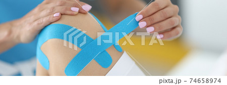 Traumatologist holds blue tape in his hand to fix patient's knee joint in clinic Traumatologist holds blue tape in his hand to fix patient's knee joint in clinic 74658974