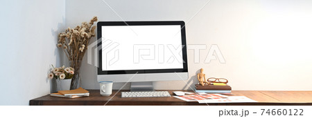 A wooden workspace is surrounding by a white blank screen computer monitor and various equipment. A wooden workspace is surrounding by a white blank screen computer monitor and various equipment. 74660122