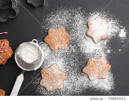 Star shaped baked gingerbread cookies sprinkled with powdered sugar on a black table 74665031