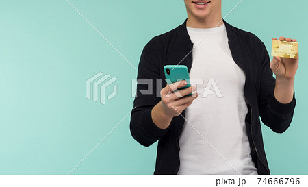 Cheerful sports guy conducts online payment and looks at the smartphone screen on a blue background. Cheerful sports guy conducts online payment and looks at the smartphone screen on a blue background. 74666796