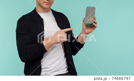 Cheerful sporty guy shows a finger on the smartphone screen on a blue background. Cheerful sporty guy shows a finger on the smartphone screen on a blue background. 74666797