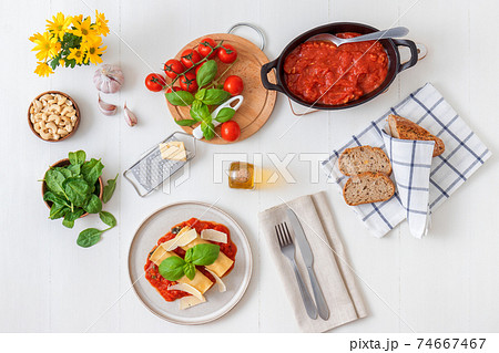 Cannelloni stuffed with spinach, feta cheese and cashew nuts with tomato and garlic sauce, embellished with parmesan cheese shavings and basil leaves. All on white wooden table background. 74667467