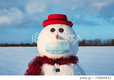 Funny snowman in stylish red hat with medical mask 74668932