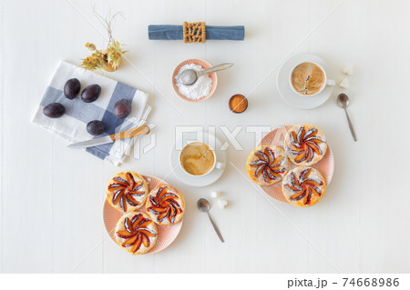Plate with plum tarts with cinnamon and icing sugar on white wooden table, tasty puff pastry dessert. Plate with plum tarts with cinnamon and icing sugar on white wooden table, tasty puff pastry dessert. 74668986