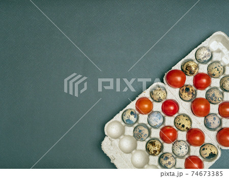 The cherry tomatoes and quail eggs are placed staggered to the egg tray over the gray background. Flat lay, close-up. The cherry tomatoes and quail eggs are placed staggered to the egg tray over the gray background. Flat lay, close-up. 74673385