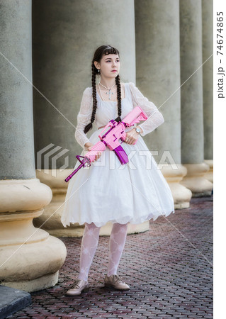 Girl in a white dress with a pink rifle plays airsoft 74674865