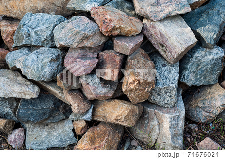 Roughly heaped granite stones, outdoor weathered material, large building blocks. Close-up. 74676024