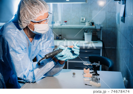 A masked and gloved dental technician works on a prosthetic tooth in his lab A masked and gloved dental technician works on a prosthetic tooth in his lab 74678474