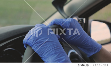 The girl hands in medical blue gloves turns the steering wheel of the car. Protection against the Covid-19 virus. Pandemic. Close-up 74679264