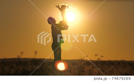 Silhouette dad throws happy little daughter into the sunset sky. Father's day. The child wants to fly above the ground. A parent with a child plays at dawn. Family and childhood concept. Kid jumps on 74679269