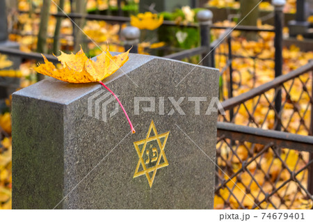 Autumn Jewish Cemetery. A yellow Maple Leaf is lying on a cemetery plate with an engraved Star of David.  74679401