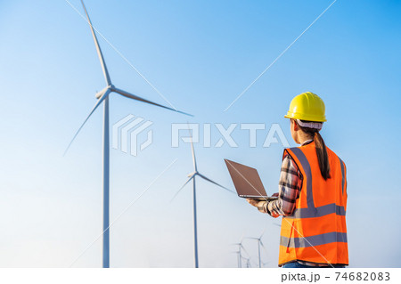 female engineer working with laptop computer against wind turbine farm female engineer working with laptop computer against wind turbine farm 74682083