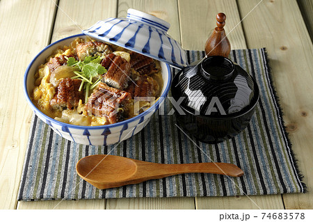 ランチョンマットの上の鰻蒲焼きを卵でとじたうな玉丼とお吸い物のセットと木製スプーン 74683578