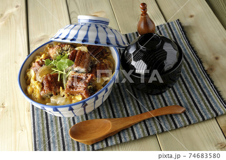 ランチョンマットの上の鰻蒲焼きを卵でとじたうな玉丼とお吸い物のセットと木製スプーン 74683580