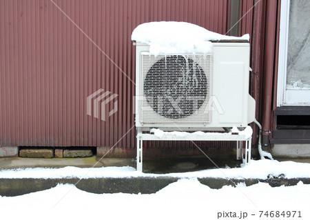 トタンの外壁と雪の積もった室外機 74684971