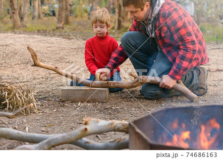 Father helping his son to cut a log for a camp fire 74686163
