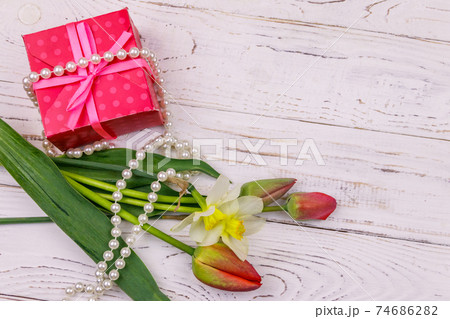 Gift box, pearl necklace and bouquet of red tulips and daffodils on wooden background. Concept of Valentine's Day, Women's Day, Mother's Day and Birthday. Top view, copy space 74686282