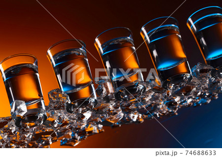 Glasses of vodka with ice on a glass table. 74688633