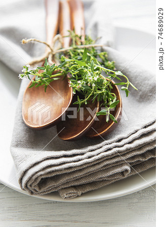 Wooden spoons on a plate and linen napkins decorated with green bunches of thyme Wooden spoons on a plate and linen napkins decorated with green bunches of thyme 74689029