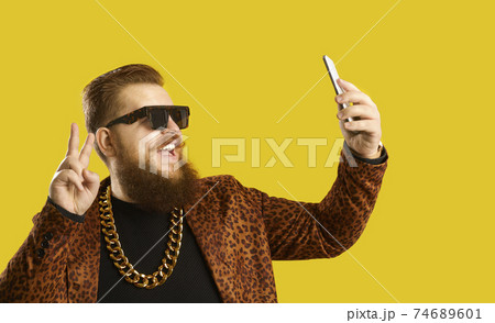 Happy man in an extravagant outfit taking a selfie or live streaming on a smartphone 74689601