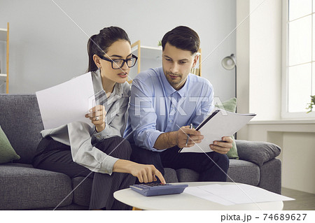 Young couple sitting on sofa, filling out tax declaration or looking through utility bills Young couple sitting on sofa, filling out tax declaration or looking through utility bills 74689627