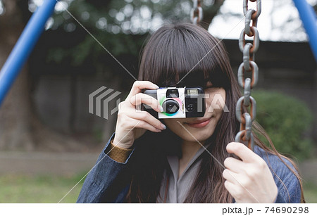 公園のブランコでインスタントカメラを持って写真を撮るロングヘアの女性のアップ 公園のブランコでインスタントカメラを持って写真を撮るロングヘアの女性のアップ 74690298