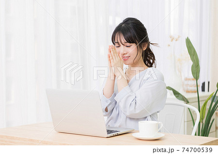 部屋でノートパソコンを使いながらお願いのジェスチャーをする若い女性 74700539