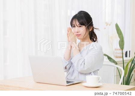 部屋でノートパソコンを使いながらお願いのジェスチャーをする若い女性 部屋でノートパソコンを使いながらお願いのジェスチャーをする若い女性 74700542