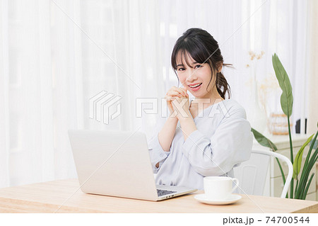 部屋でノートパソコンを使いながらお願いのジェスチャーをする若い女性 部屋でノートパソコンを使いながらお願いのジェスチャーをする若い女性 74700544