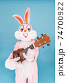 Positive funny musician guitarist plays music by ukulele or Hawaiian guitar isolated on blue. Easter bunny or rabbit or hare celebrates Happy easter 74700922