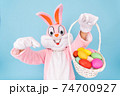 Easter bunny or rabbit or hare with basket of colored eggs, shows thumb finger up, having fun, dancing, celebrates Happy easter. Easter rabbit isolated on blue background 74700927