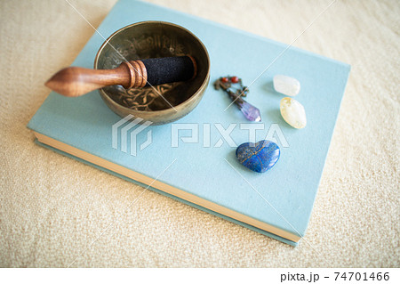 本の上に置かれたシンギングボウルとアメジストのペンデュラム、パワーストーン。 74701466