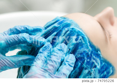 Hairdresser in protective gloves washes client's blue hair with shampoo for washing after process of coloring hair in sapphire color Hairdresser in protective gloves washes client's blue hair with shampoo for washing after process of coloring hair in sapphire color 74705226