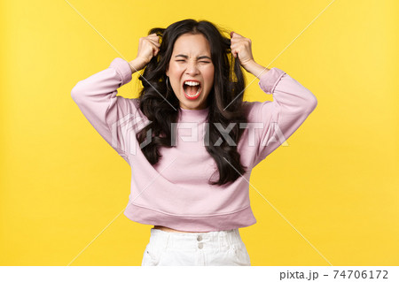 Lifestyle, emotions and advertisement concept. Angry distressed asian woman screaming hateful and outraged, feeling pissed-off and fed up, pulling her hair with anger and rage, yellow background 74706172