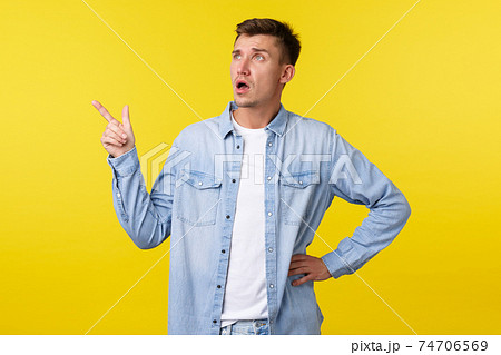 Confused and surprised startled handsome adult man asking question about product, looking and pointing finger upper left corner, consulting shop clerk, standing yellow background 74706569