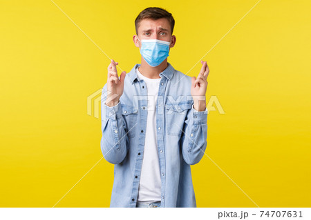 Concept of covid-19 pandemic outbreak, lifestyle during coronavirus social distancing. Hopeful desperate blong guy in medical mask, feeling nervous cross fingers good luck, awaiting important news Concept of covid-19 pandemic outbreak, lifestyle during coronavirus social distancing. Hopeful desperate blong guy in medical mask, feeling nervous cross fingers good luck, awaiting important news 74707631