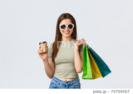 Shopping mall, lifestyle, tourism and fashion concept. Stylish carefree woman in sunglasses, drinking coffee and purchase clothes, holding takeaway cup and shop bags 74709567