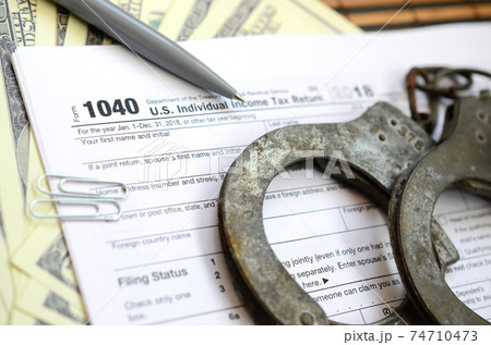 Police handcuffs lie on the tax form 1040. The concept of problems with the law in the aftermath of non-payment of taxes 74710473