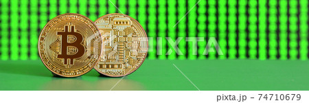 Two gold bitcoins lie on the green surface on the background of the display, which shows the process of mining the crypto currency 74710679