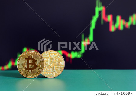 Two gold bitcoins lie on the green surface on the background of the display, which depicts the growth of the position on the chart Two gold bitcoins lie on the green surface on the background of the display, which depicts the growth of the position on the chart 74710697