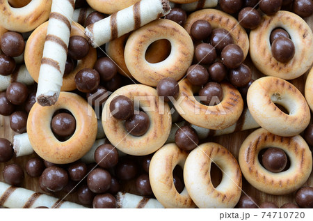 A lot of crispy sweet tubules, chocolate melting balls and yellow bagels lie on a wooden surface. Close up view A lot of crispy sweet tubules, chocolate melting balls and yellow bagels lie on a wooden surface. Close up view 74710720