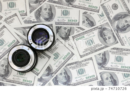 Two photographic lenses lie on the background of a lot of dollar bills. Space for text 74710726