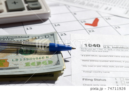 1040 Individual Income Tax Return blank with dollar bills, calculator and pen on calendar page with marked 15th April 74711926
