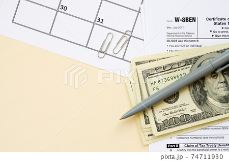 IRS Form W-8BEN Certificate of foreign status of beneficial owner for United States tax withholding and reporting for individuals blank lies with pen and hundred dollar bills on calendar page 74711930