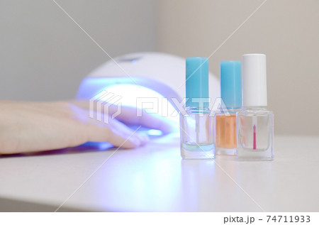 Three colorless transparent nail polish bottles in background of female hands in gel uv led nail white lamp for drying manicure 74711933