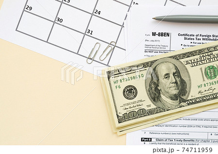 IRS Form W-8BEN Certificate of foreign status of beneficial owner for United States tax withholding and reporting for individuals blank lies with pen and hundred dollar bills on calendar page 74711959