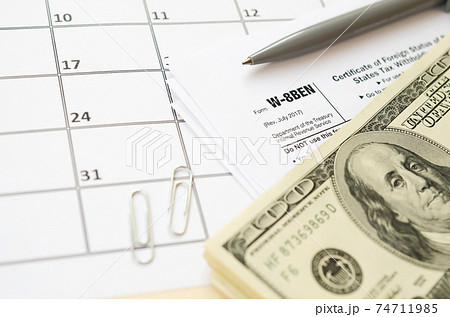 IRS Form W-8BEN Certificate of foreign status of beneficial owner for United States tax withholding and reporting for individuals blank lies with pen and hundred dollar bills on calendar page 74711985