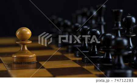 One white pawn against an army of black pieces on a chessboard 74712283